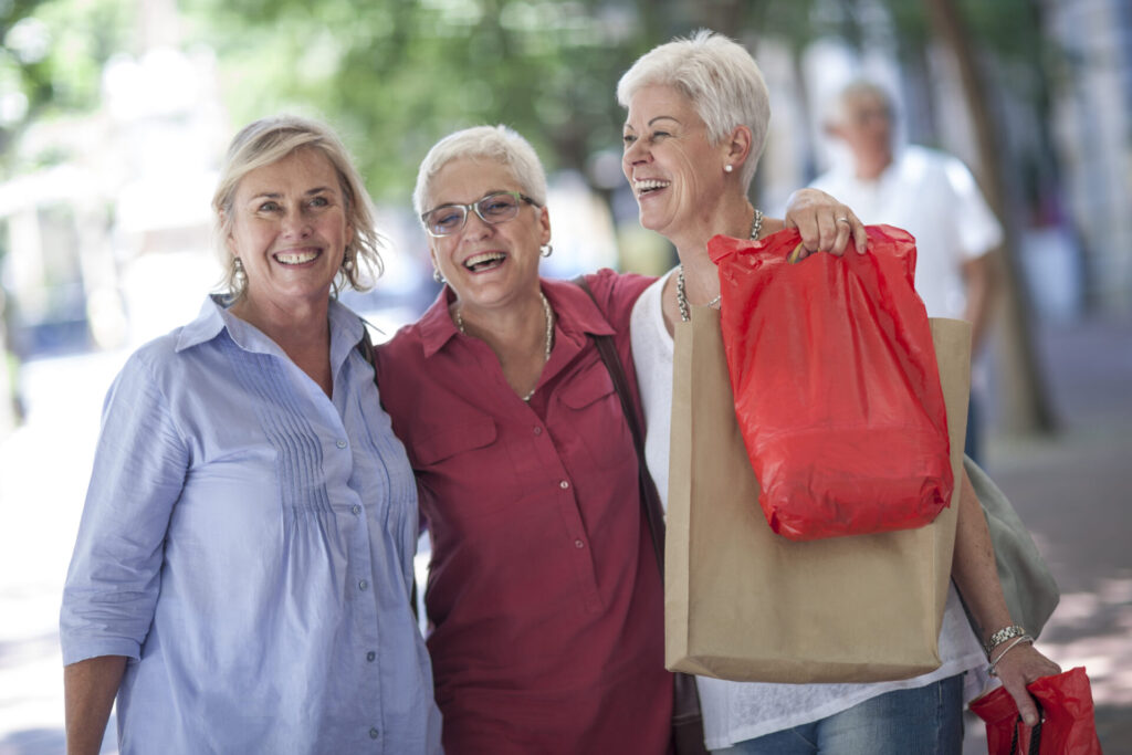 Three smiling older women holding shopping bags and laughing together during a day out.