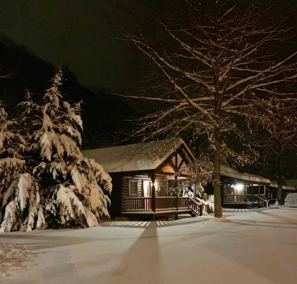 Small log cabins at night with snow covering the ground and roofline.